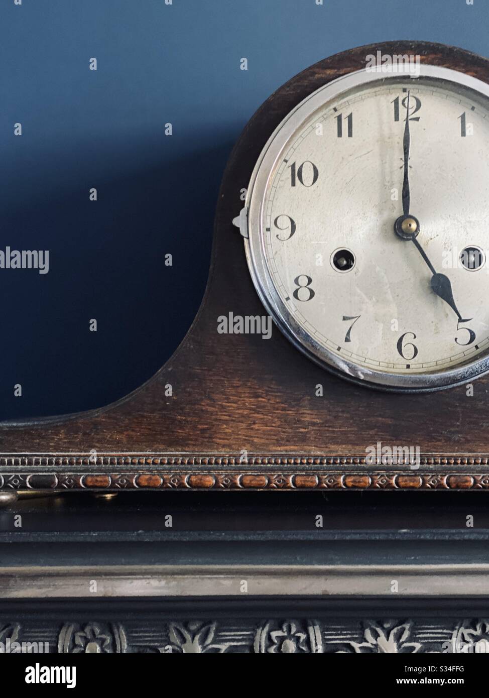 An antique Mantel clock on a mantel piece against a blue wall
