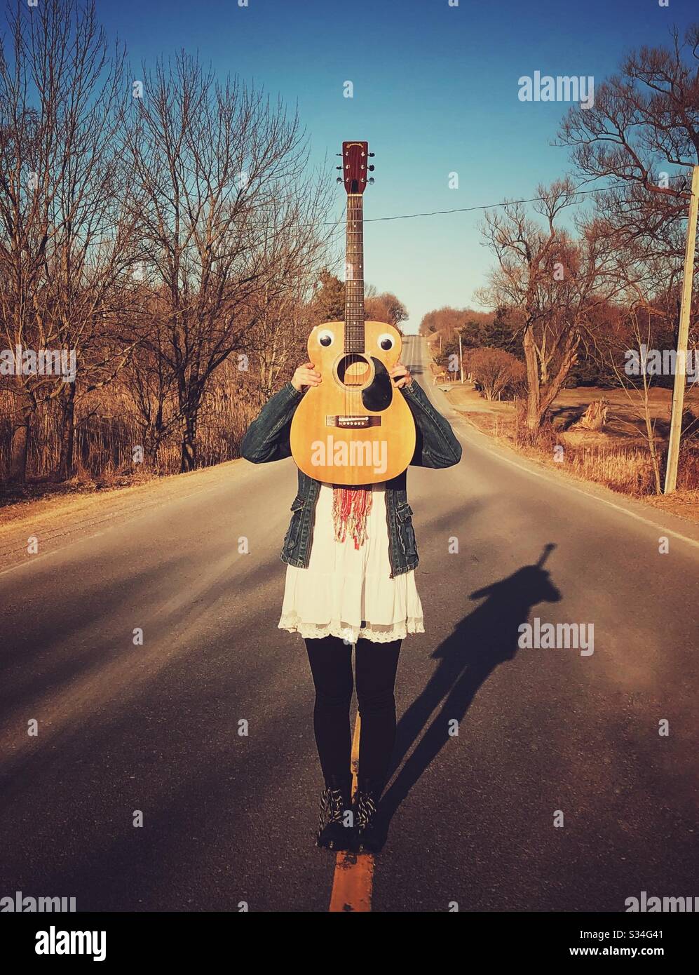 Teen girl holding wooden acoustic guitar in front of face - Smartphone Captured Stock Image