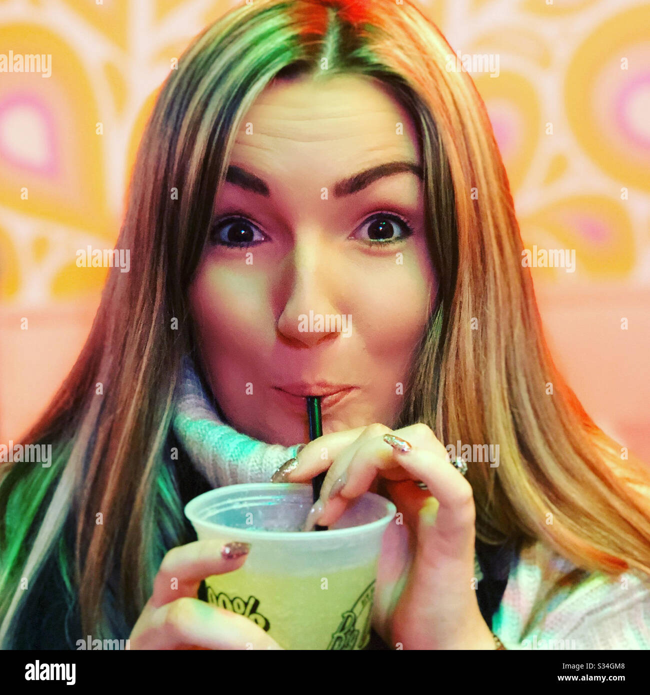 Blonde woman in retro American diner drinking through a straw Stock