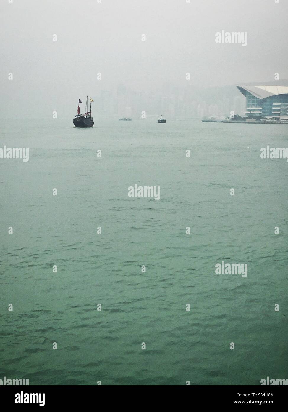 The 'Aqua Luna', a replica Chinese junk used for tourist sightseeing, on Victoria Harbour on a hazy day in Hong Kong - Smartphone Captured Stock Image