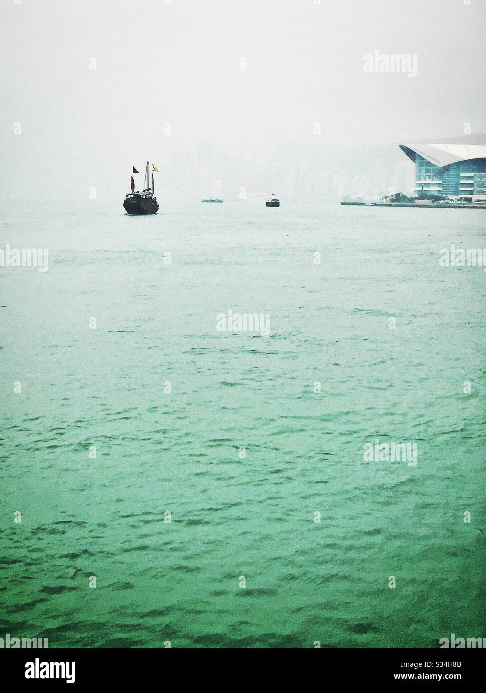 The 'Aqua Luna', a replica Chinese junk used for tourist sightseeing, on Victoria Harbour on a hazy day in Hong Kong - Smartphone Captured Stock Image