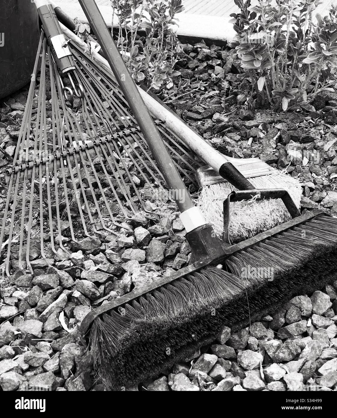 Garden maintenance, cleaning, tools, rake, big broom, small broom, plants, rocks, black white filter, closeup, landscape work Stock Photo