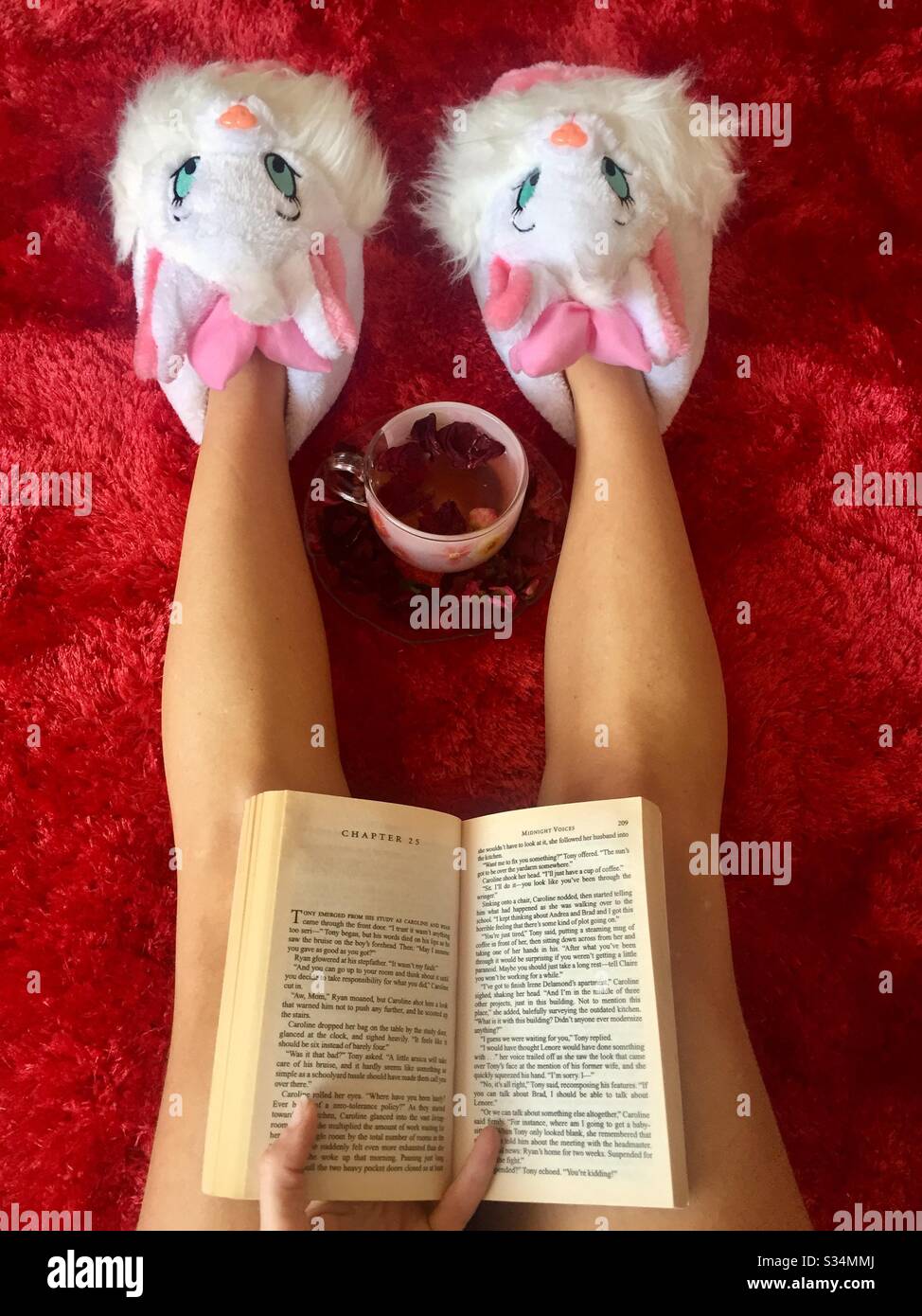 Woman wearing funny face shoes reading a book while lying down on the carpet - Smartphone Captured Stock Image