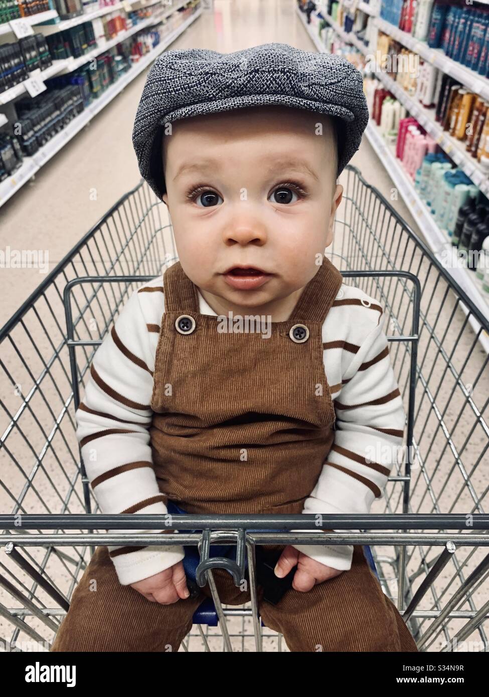 Baby in Yorkshire flat cap shopping trolly Stock Photo