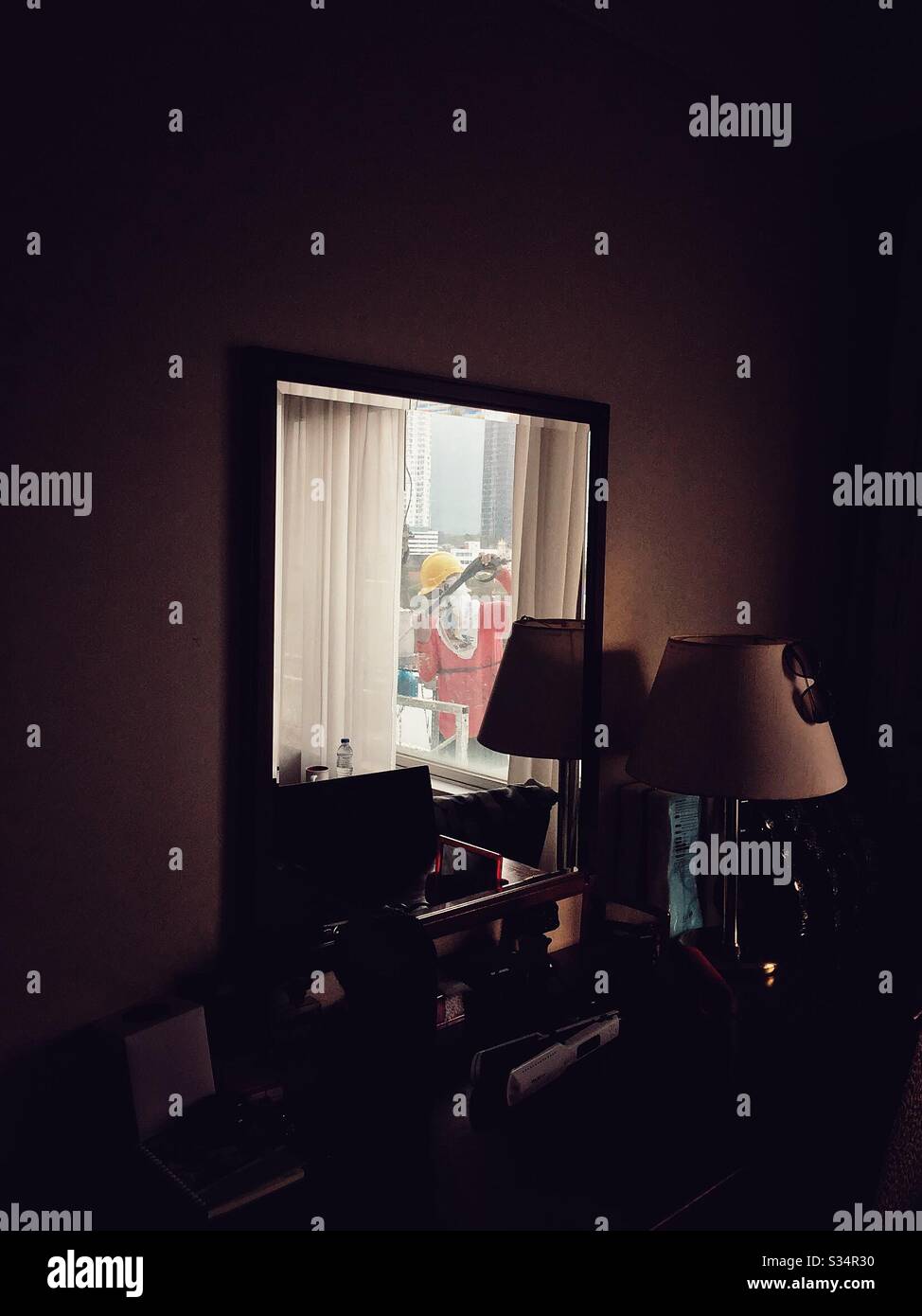 A reflection of a man on the mirror cleaning the window outside of a hotel room. - Smartphone Captured Stock Image