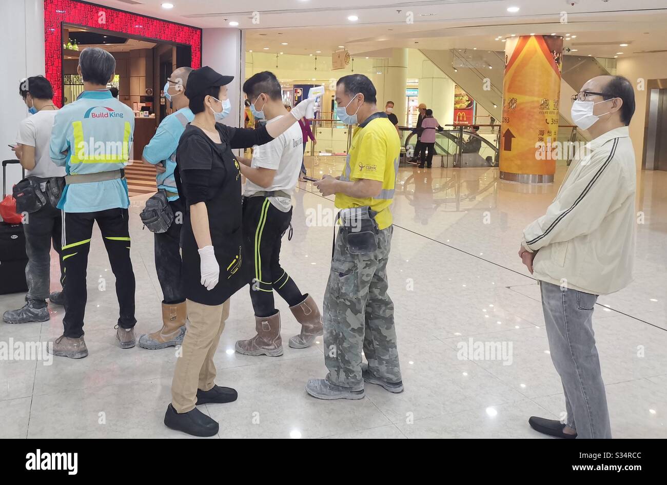 Hongkongers wearing masks and their fever being checked while waiting in line in a restaurant during the Covid-19 pandemic. - Smartphone Captured Stock Image
