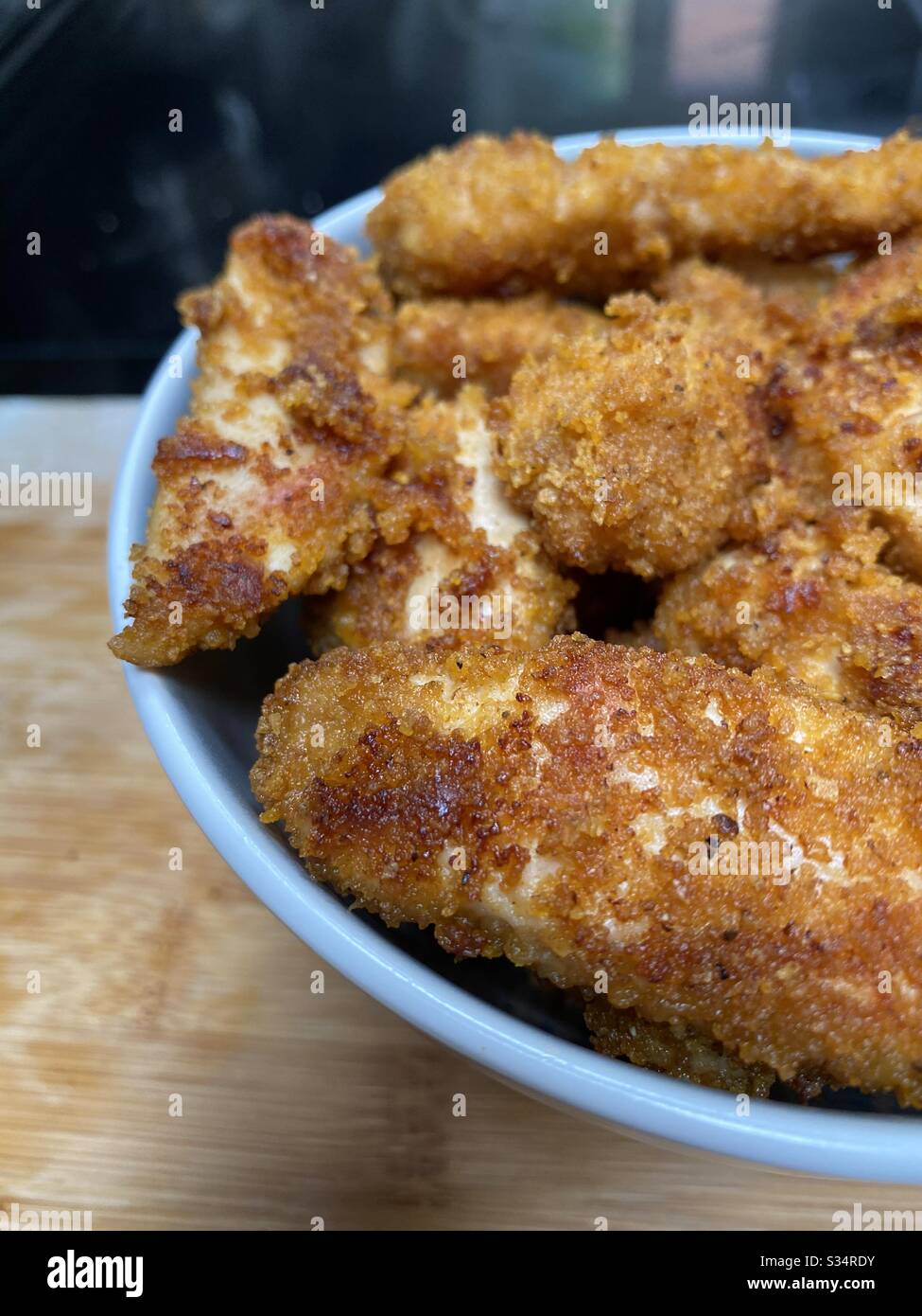Closeup of homemade chicken nuggets/goujons in bowl on bamboo chopping board Stock Photo