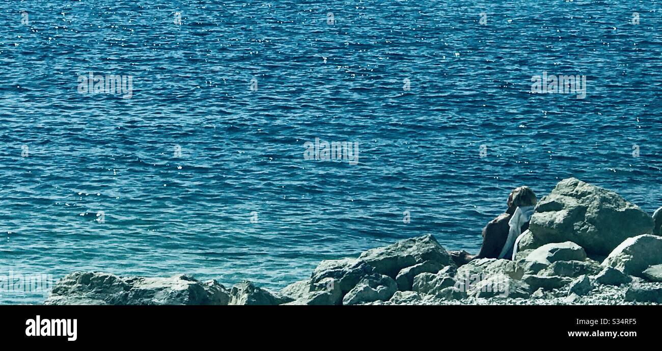 A man is sunbathing hidden among the rocks during corona virus times in Splir, Croatia - Smartphone Captured Stock Image