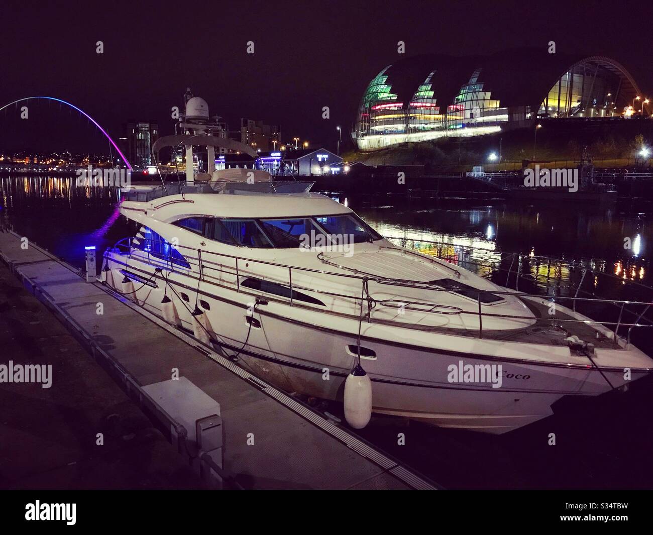 Architecture of Newcastle Quayside lit up by night. Newcastle upon Tyne, North East England. A luxury yacht moored at Newcastle City Marina on the River Tyne with Sage Gateshead and Millennium Bridge - Smartphone Captured Stock Image