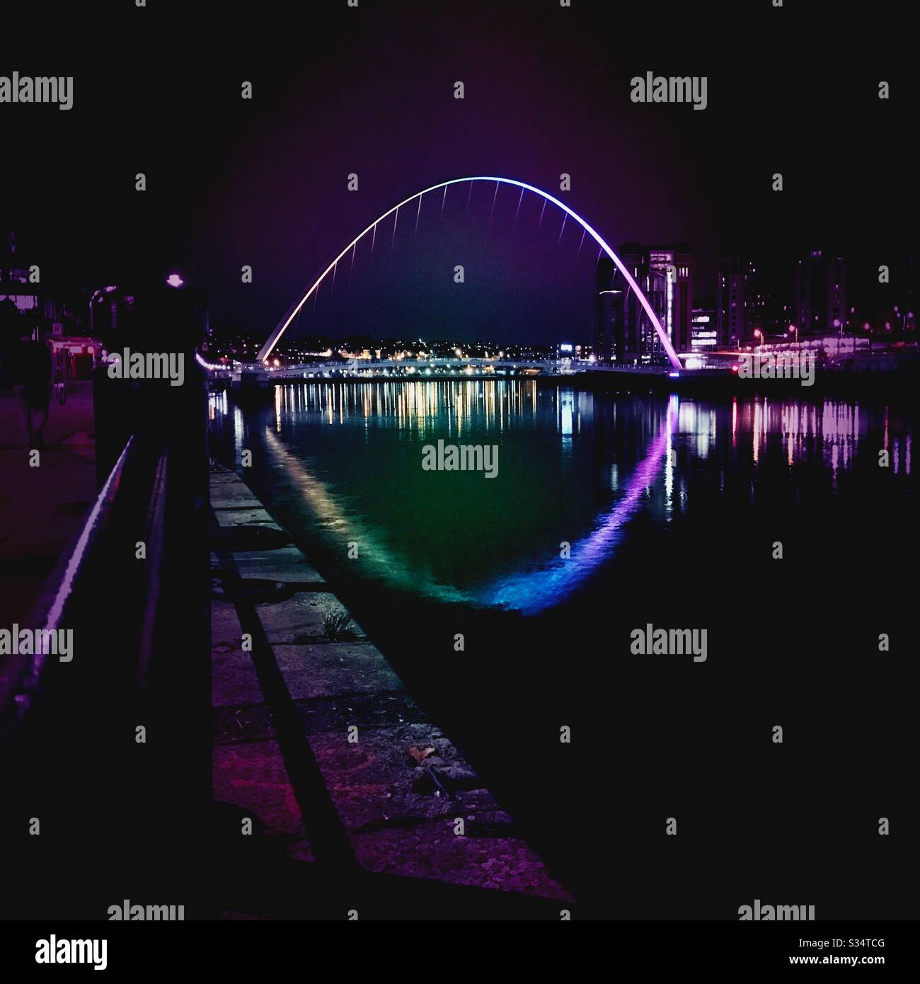 Architecture of Newcastle Quayside lit up by night. Newcastle upon Tyne, North East England. The Millennium Bridge reflecting in the River Tyne - Smartphone Captured Stock Image