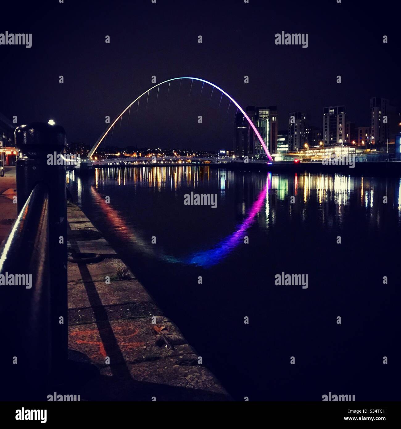 Architecture of Newcastle Quayside lit up by night. Newcastle upon Tyne, North East England. The Millennium Bridge reflecting in the River Tyne - Smartphone Captured Stock Image