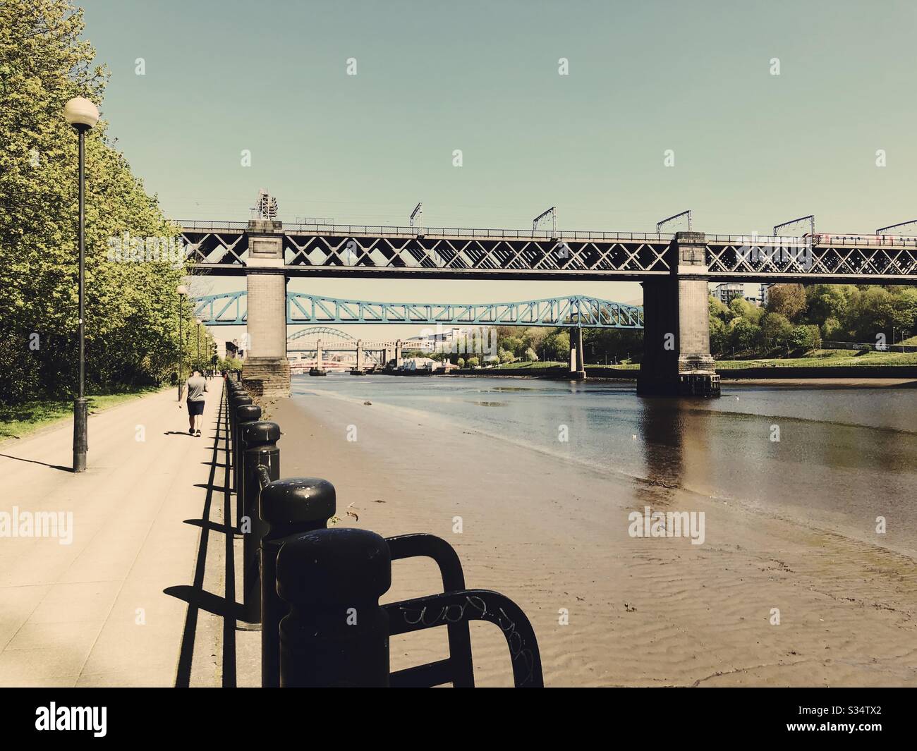 Architecture of Newcastle Quayside under a blue summer sky. Newcastle upon Tyne, North East England. King Edward steel truss railway bridge over River Tyne. Grade II Listed Structure - Smartphone Captured Stock Image