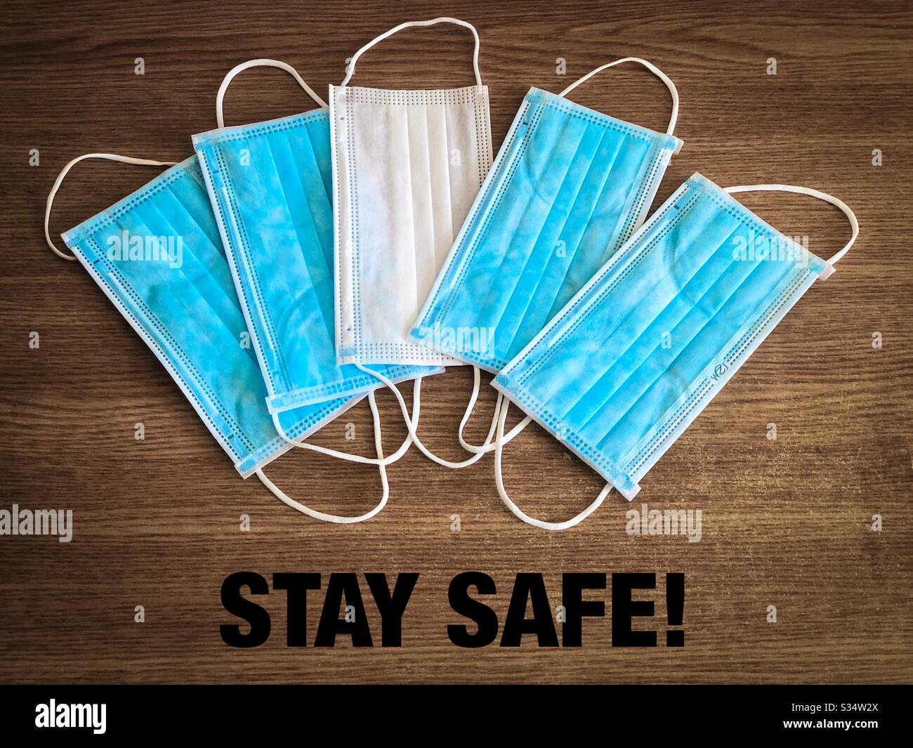 Pile of surgical masks on wooden table with the message stay safe - Smartphone Captured Stock Image