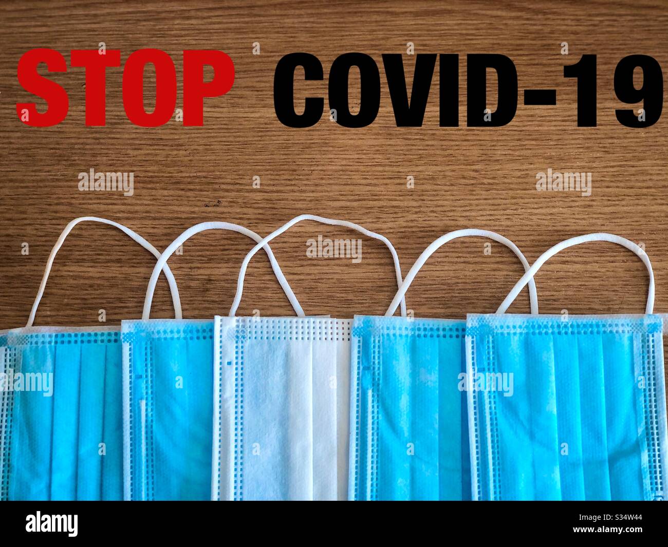 Multiple surgical masks on wooden table with the message to stop covid-19 - Smartphone Captured Stock Image