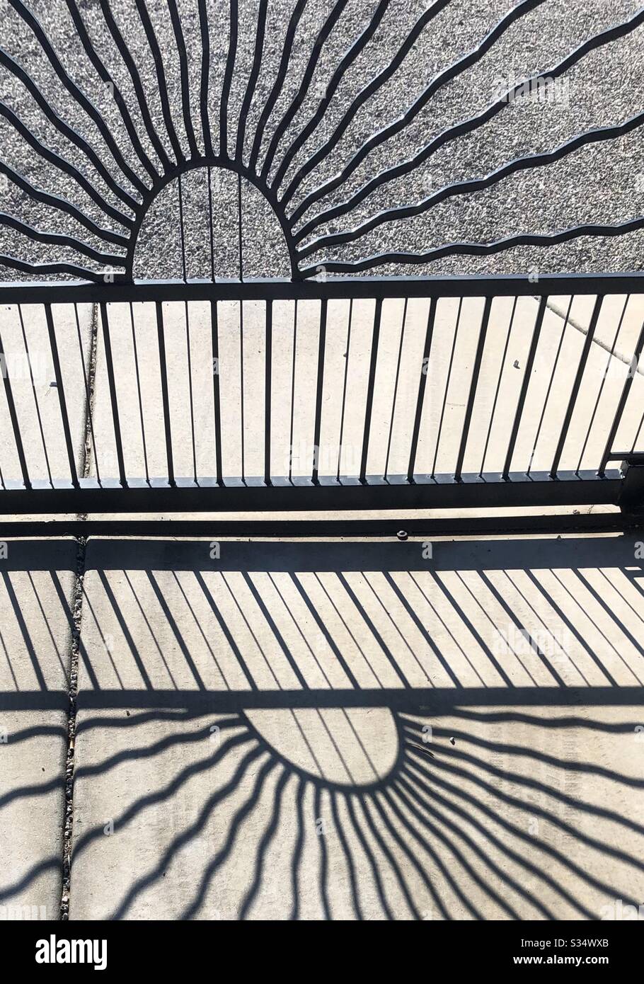 Natural light, shadows, iron gate, cement driveway, straight lines, partial circle, sunburst design, abstract Stock Photo