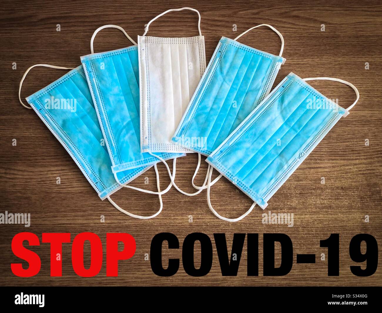 Multiple surgical masks on wooden table with the message to stop covid-19 - Smartphone Captured Stock Image