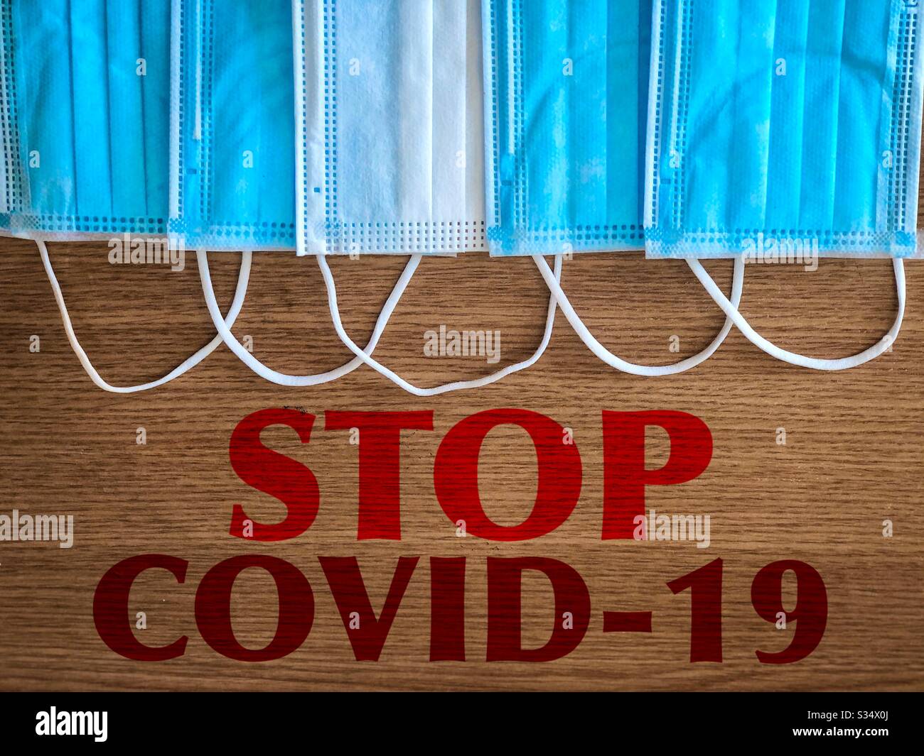 Multiple surgical masks on wooden table with the message to stop covid-19 - Smartphone Captured Stock Image