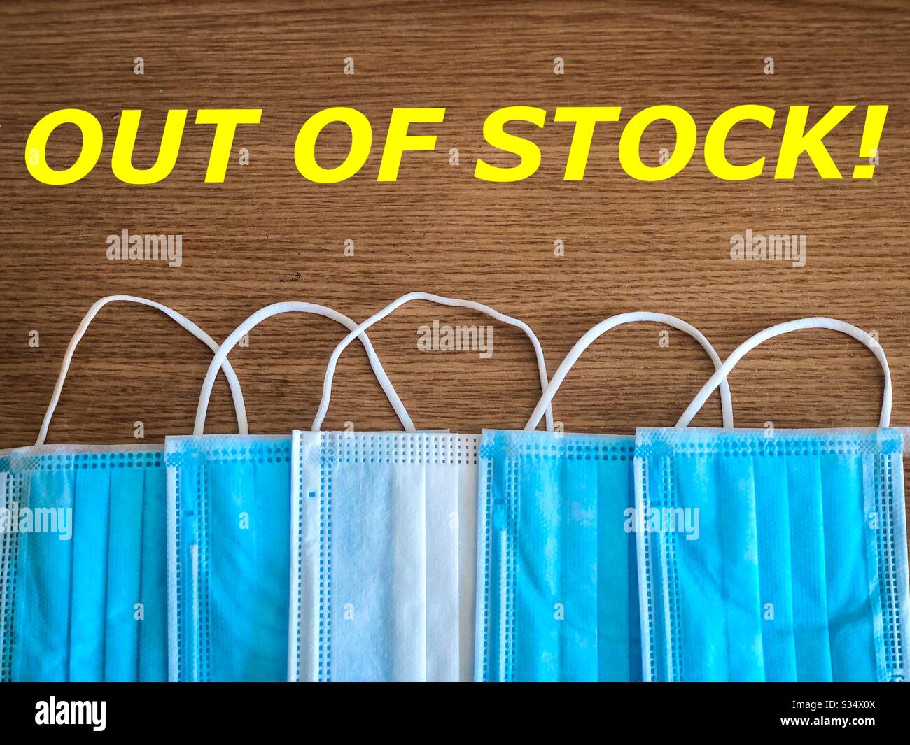 Multiple surgical masks on wooden table with the message “out of stock” - Smartphone Captured Stock Image