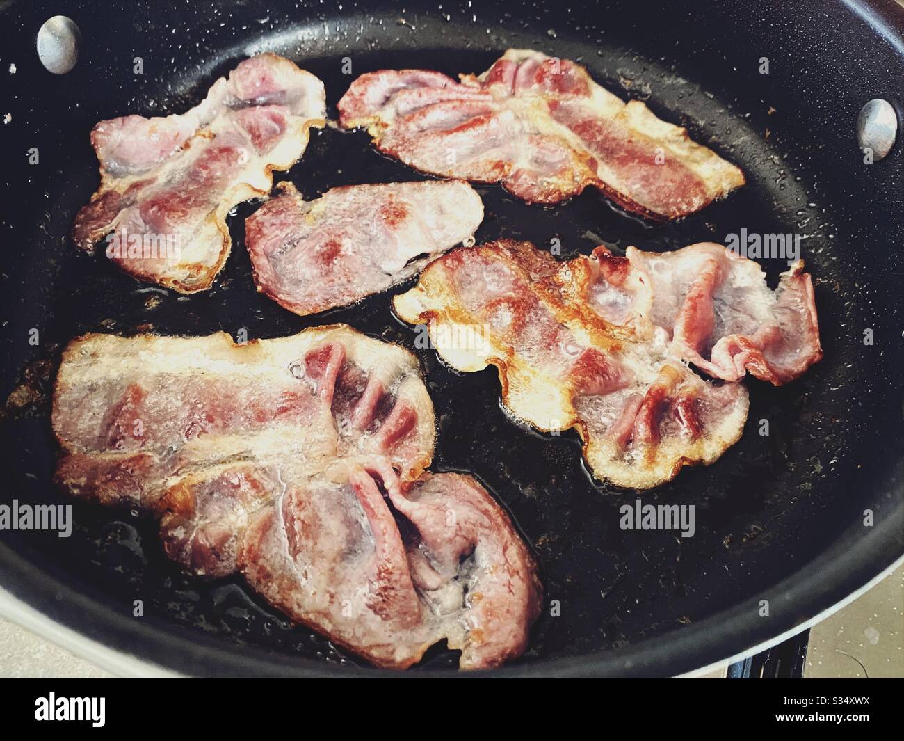 https://c8.alamy.com/comp/S34XWX/a-close-up-view-of-bacon-sizzling-in-the-frying-pan-on-a-stovetop-cooking-bacon-slices-for-breakfast-fry-up-S34XWX.jpg