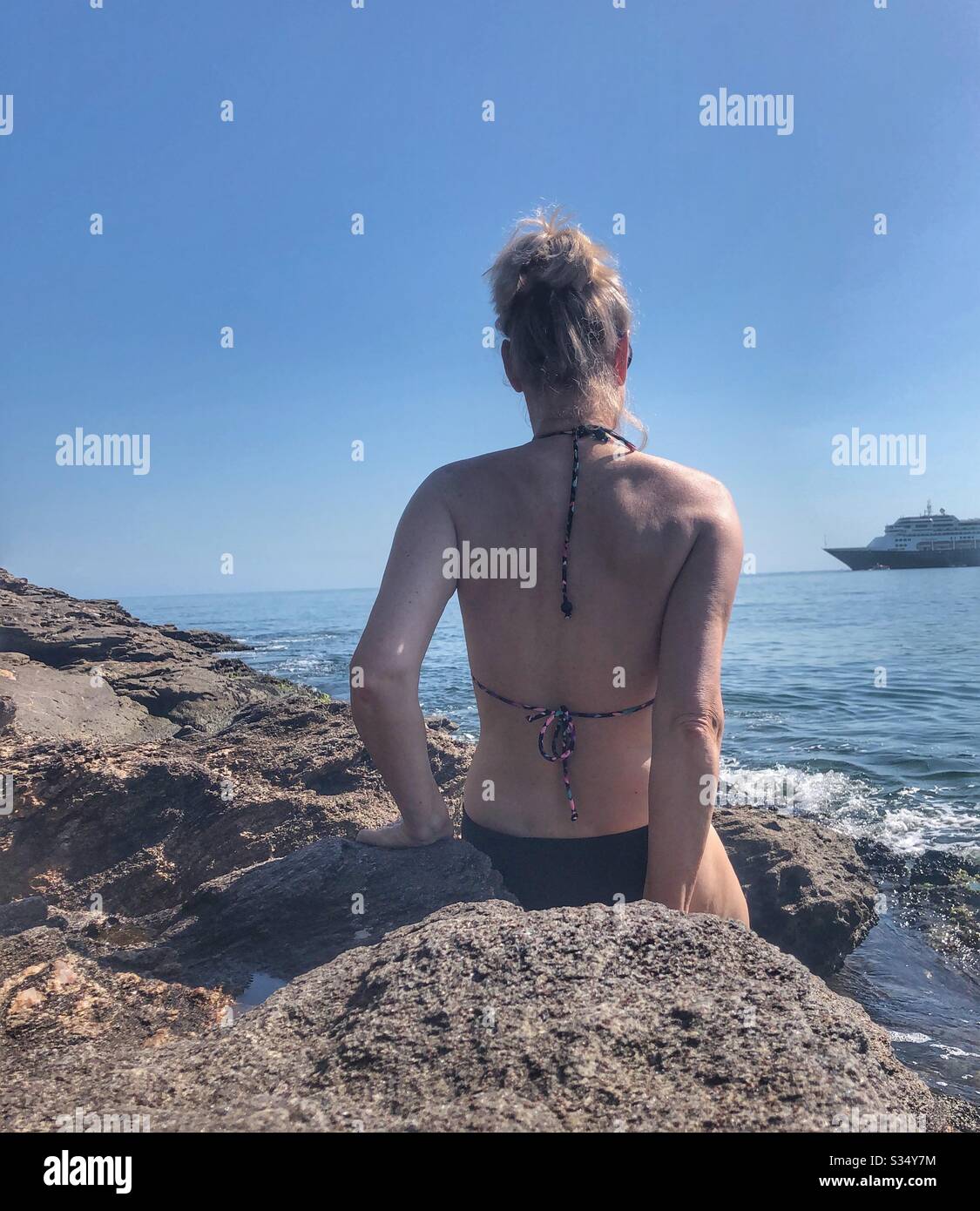 Woman sitting on a rock looking out to sea. - Smartphone Captured Stock Image