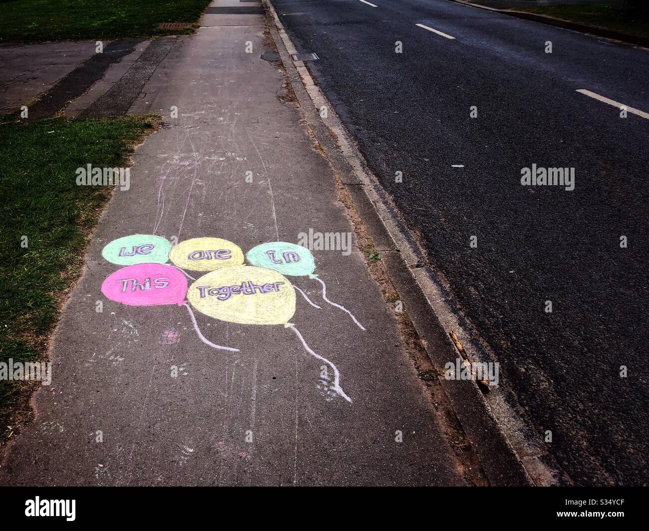 Coronavirus lockdown UK 2020 - message chalked on British pavement sidewalk - public support 'We are in this together' in balloons - Smartphone Captured Stock Image