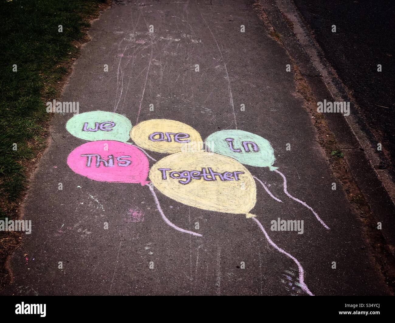 Coronavirus lockdown UK 2020 - message chalked on British pavement sidewalk - public support 'We are in this together' in balloons - Smartphone Captured Stock Image