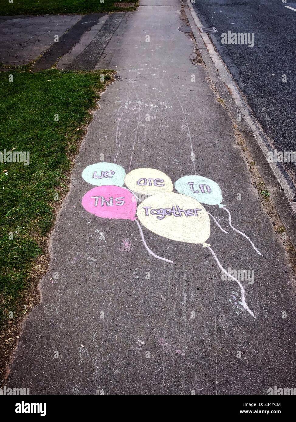Coronavirus lockdown UK 2020 - message chalked on British pavement sidewalk - public support 'We are in this together' in balloons - Smartphone Captured Stock Image