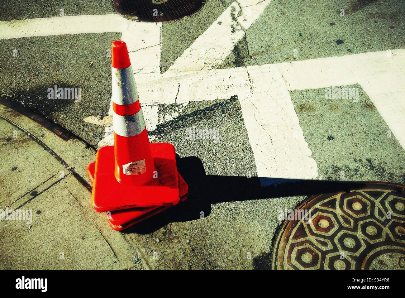 Pair of Safety Cones Stacked on Curb Next to Manhole Cover with Long Shadow Stock Photo