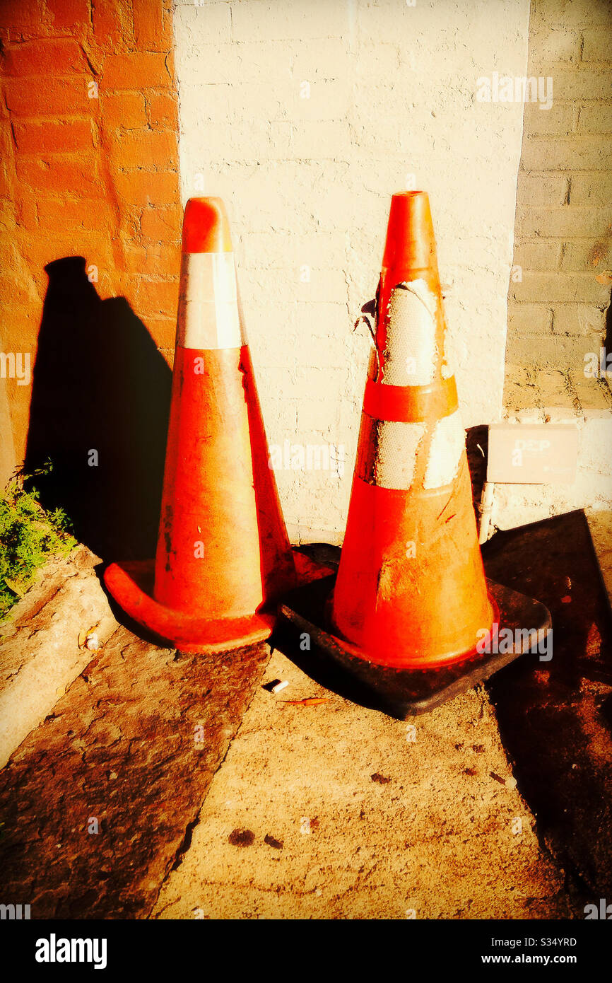 Pair of Safety Cones by Brick Wall in Late Afternoon Sunlight Stock Photo