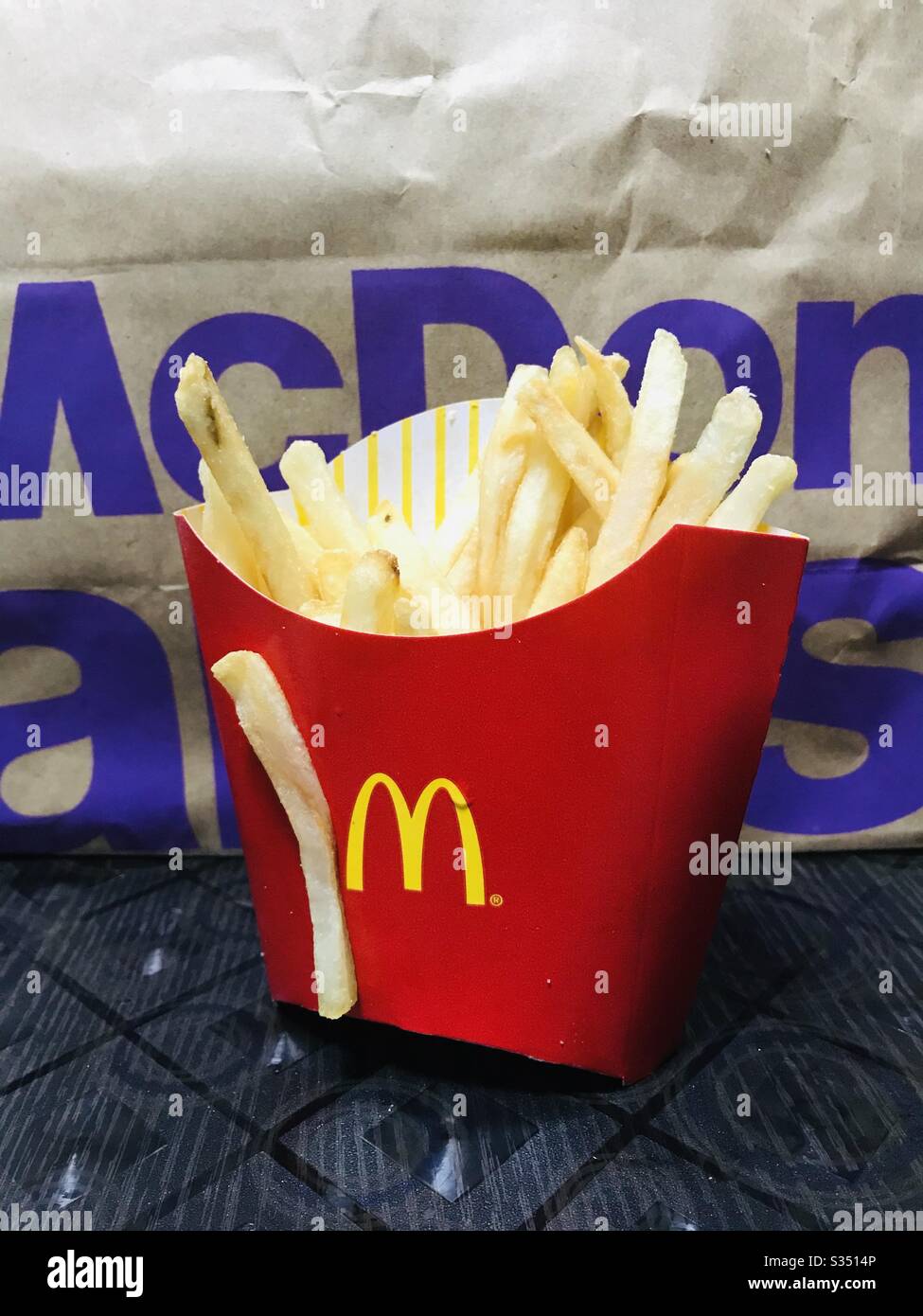 A portion of McDonald’s French fries on a McD paper bag background - a single fries stick outside on the box, quickly took a snap.. yummy junk food ever, fast food quick snack anytime anywhere, Stock Photo