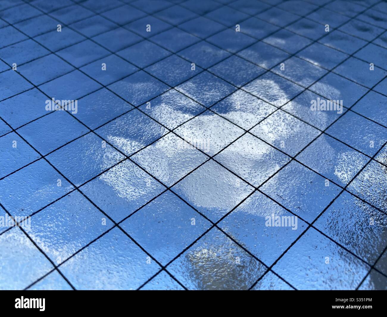 Close, angled view of opaque safety glass with wire mesh running through it, Indistinct blue sky and white cloud barely visible through it, creating abstract background texture. - Smartphone Captured Stock Image