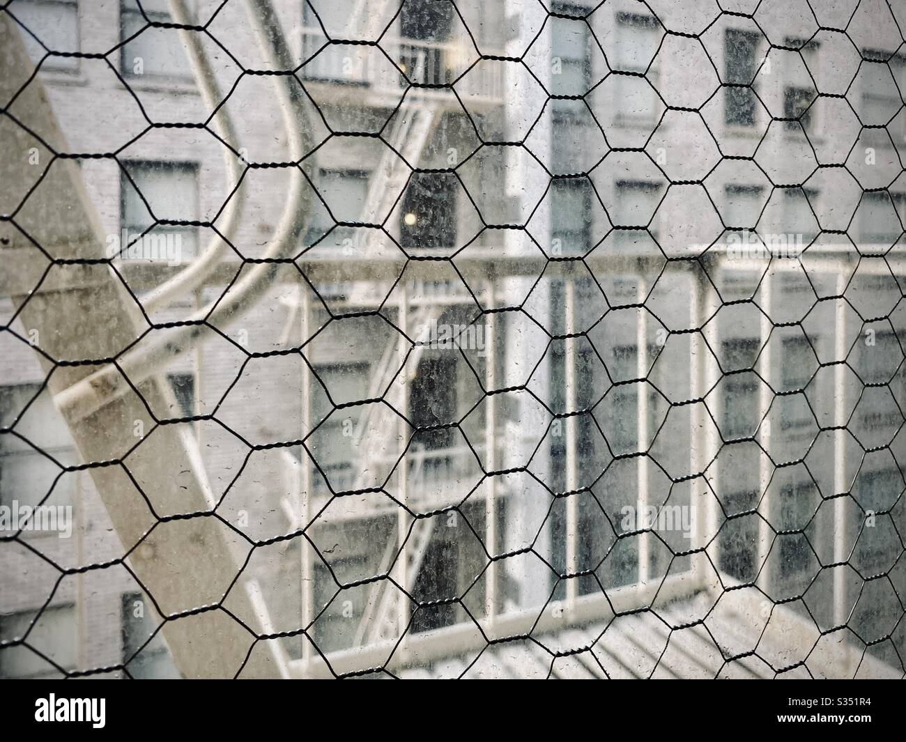 LOS ANGELES, CA, MAR 2020: fire escapes and apartment windows, in soft focus, seen through wire mesh of safety glass, focus on foreground - Smartphone Captured Stock Image