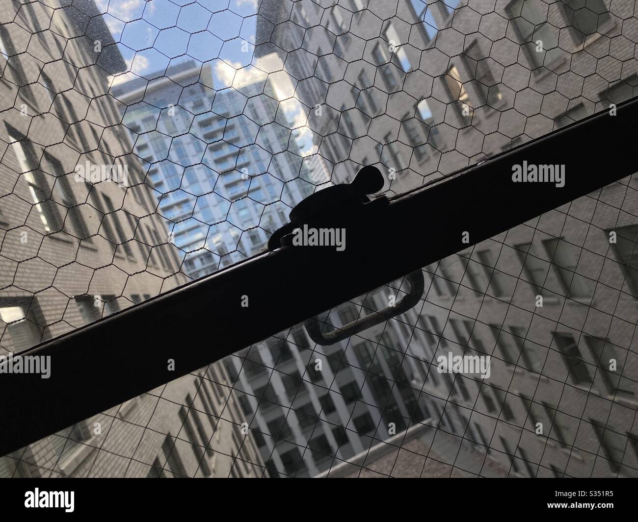 LOS ANGELES, CA, MAR 2020: angled view of apartment building windows, in soft focus, seen through wire mesh of safety glass, focus on foreground and silhouetted window lock Stock Photo