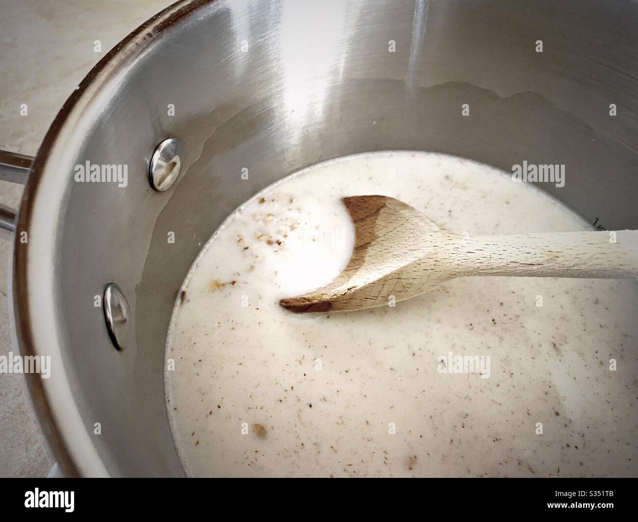 A close up view of porridge oats cooking on a gas stove. Simmering rolled oats and milk in a silver pan with milk. Healthy breakfast with wooden spoon. - Smartphone Captured Stock Image