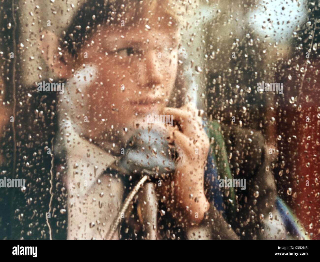 Schoolboy tries dialing old phone in London phone box on street in the rain - Smartphone Captured Stock Image