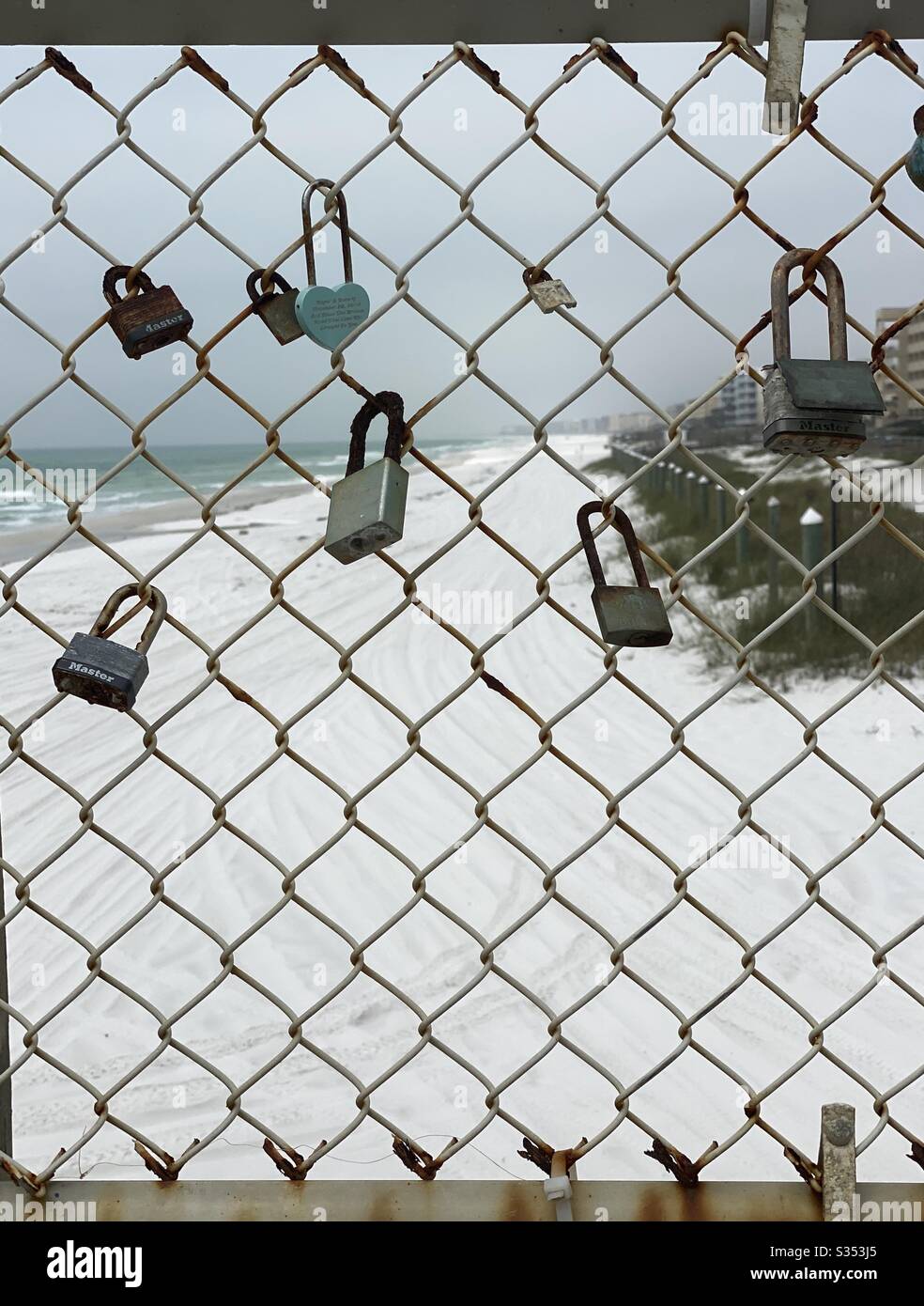 Rusty padlocks on a chain link fence with view of the beach in the background - Smartphone Captured Stock Image