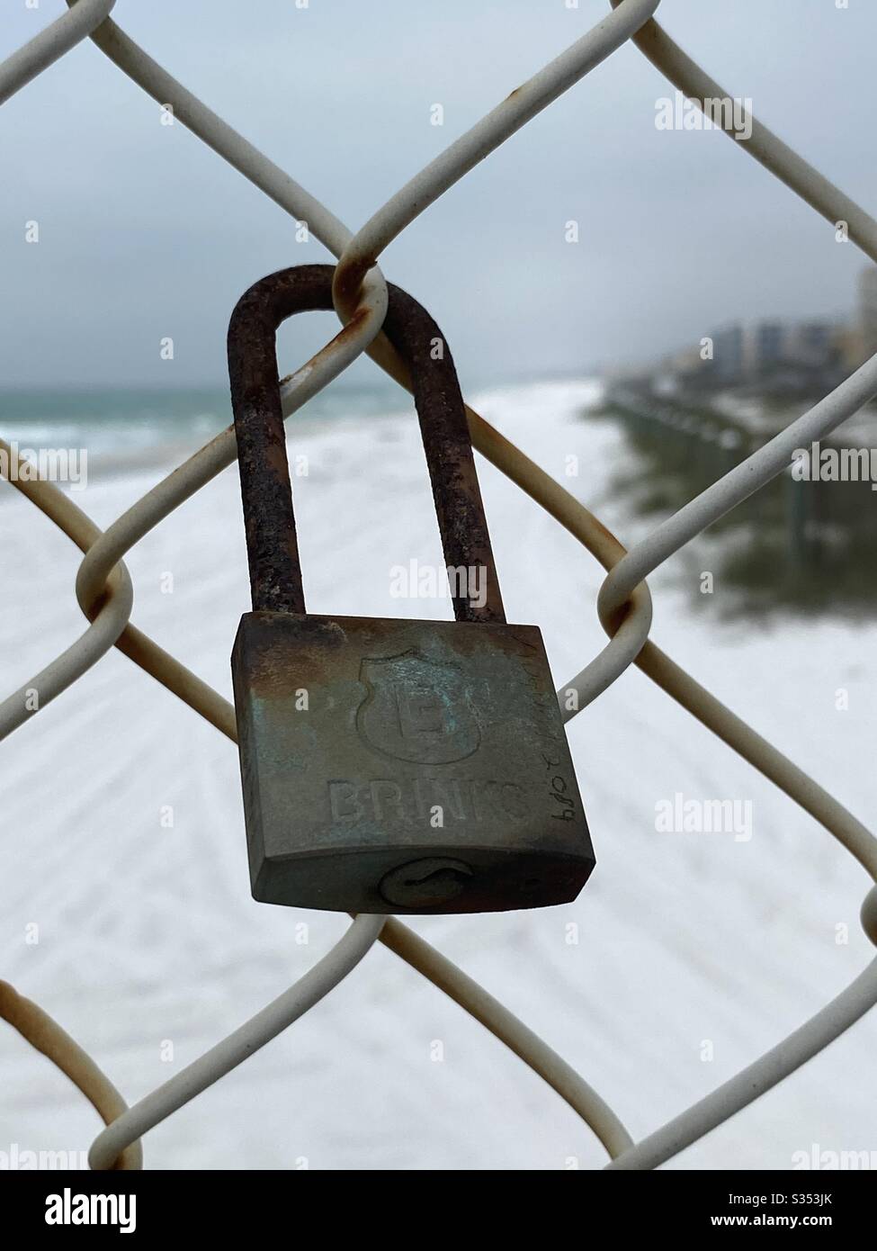 Closeup of a rusted padlock on a chain link fence with white sand beach background - Smartphone Captured Stock Image