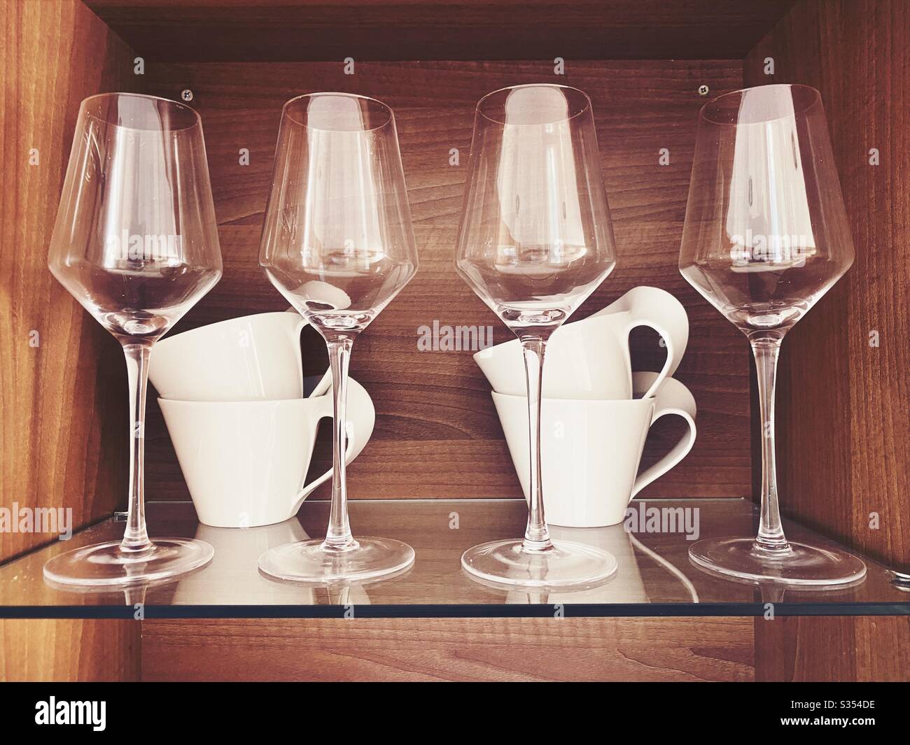 Wine glasses and contemporary cups are seen up close on a glass display shelf - Smartphone Captured Stock Image