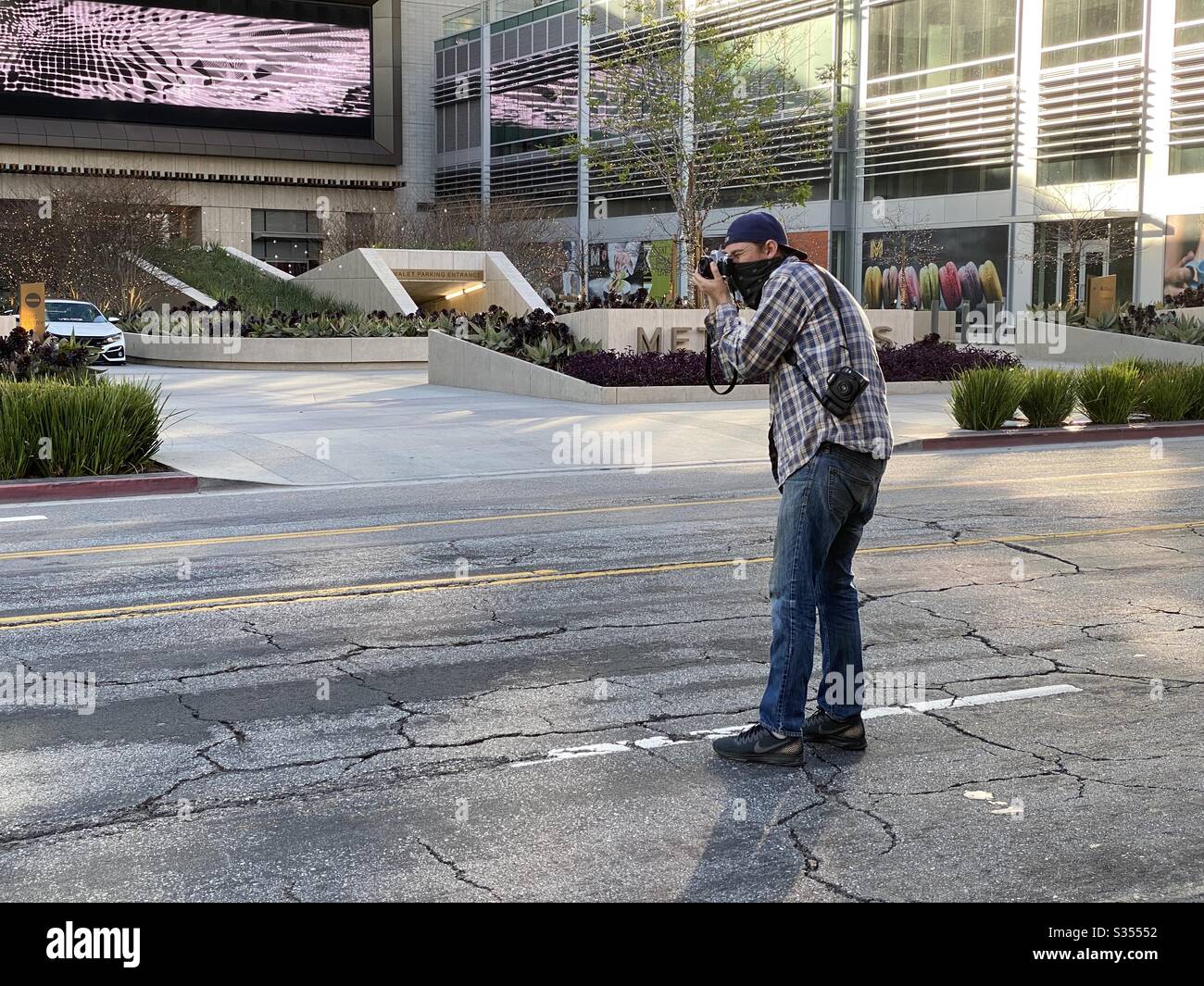 LOS ANGELES, CA, MAR 2020: Photographer wearing bandana to cover face stands in street while taking pictures in Downtown during coronavirus, Covid-19 pandemic - Smartphone Captured Stock Image