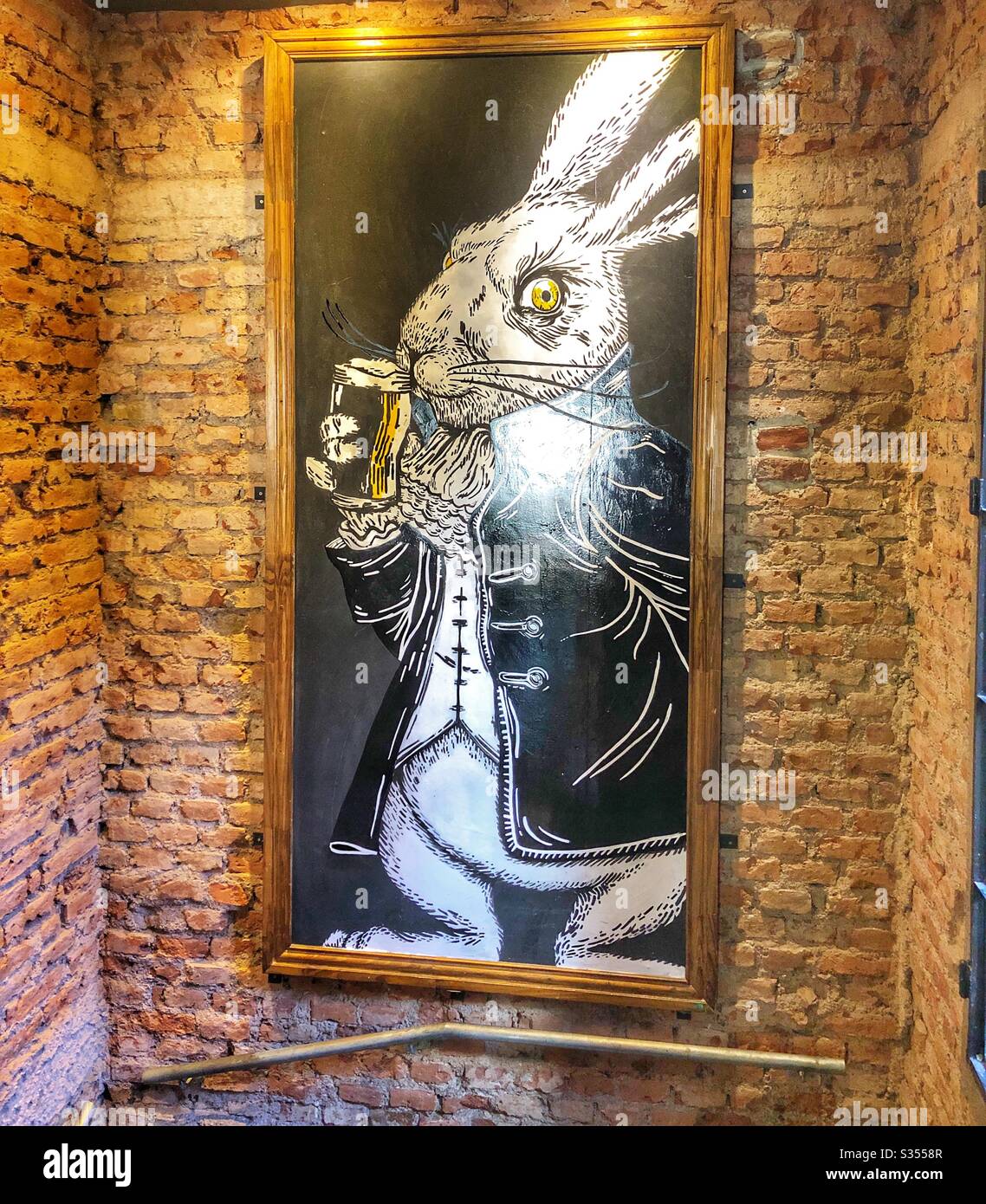 A chalkboard drawing of a rabbit drinking beer hanging on a brick wall of a restaurant. Stock Photo