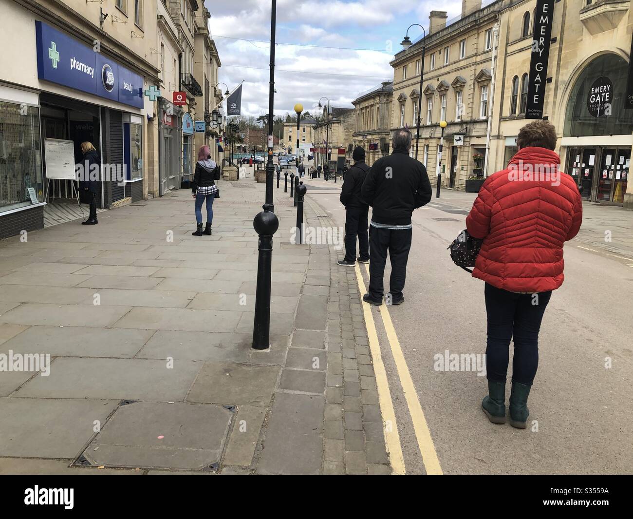 People queue outside the entrance to a pharmacy during the coronavirus lockdown in the UK - Smartphone Captured Stock Image