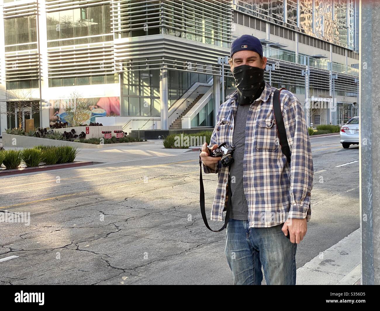 Photographer wearing bandana to cover face poses between taking pictures on streets in Downtown Los Angeles during coronavirus, Covid-19 pandemic. Identifying logos and signage removed Stock Photo
