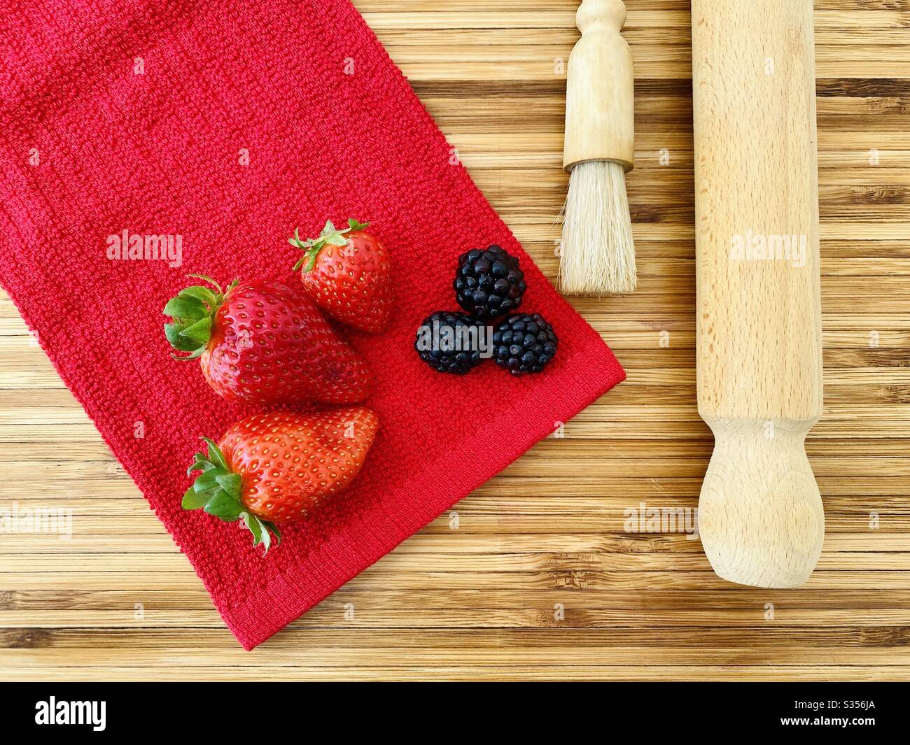 Strawberries and blackberries on a wooden kitchen counter. Ingredients for baking a summer berry, strawberry and blackberry pie. - Smartphone Captured Stock Image