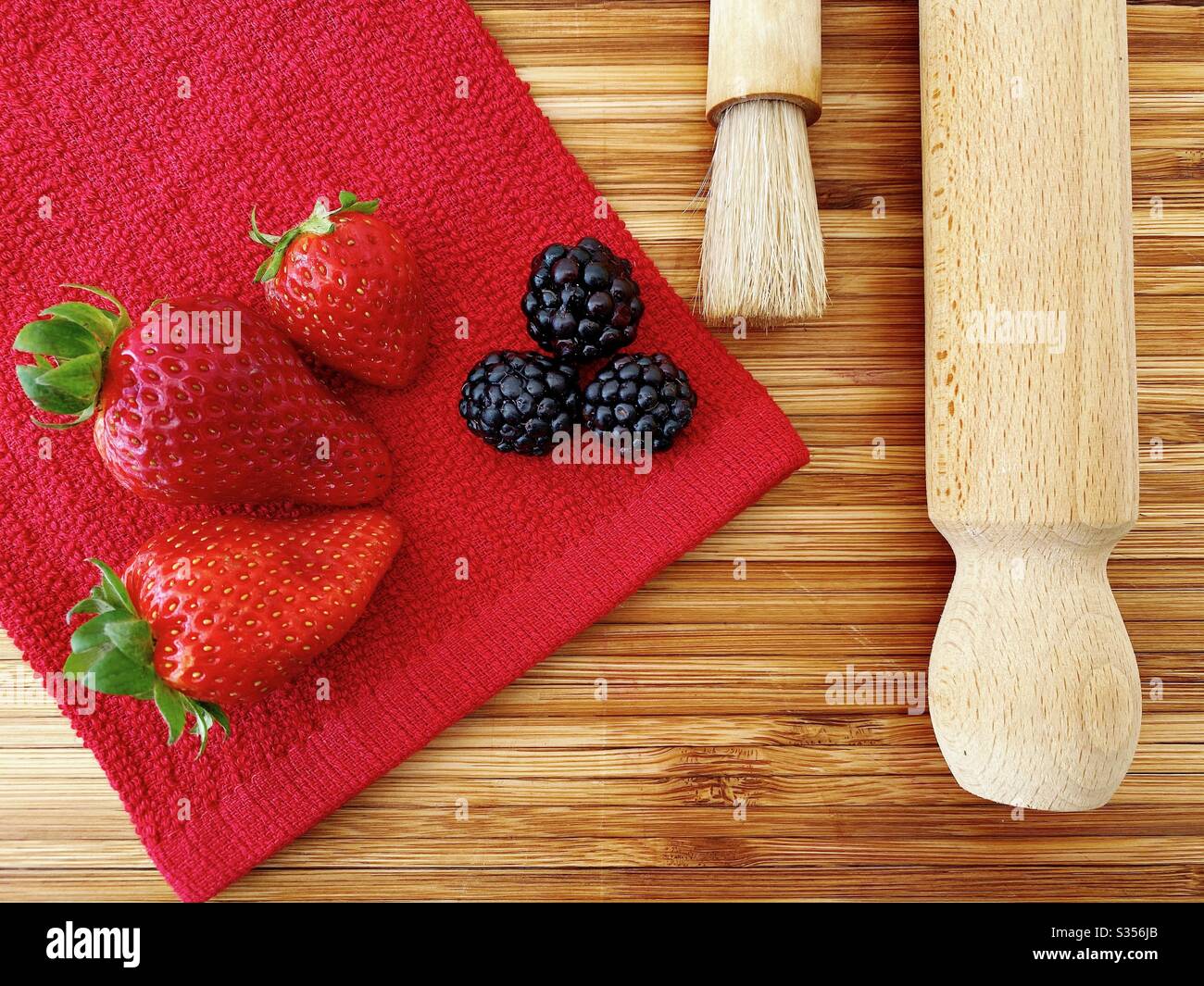 Strawberries and blackberries on a wooden kitchen counter. Ingredients for baking a summer berry, strawberry and blackberry pie. - Smartphone Captured Stock Image