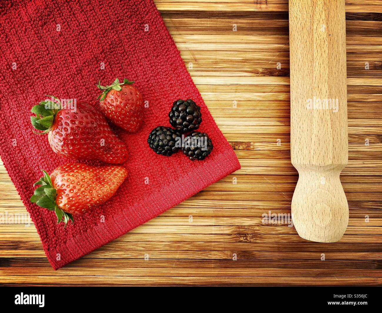 Strawberries and blackberries on a wooden kitchen counter. Ingredients for baking a summer berry, strawberry and blackberry pie. - Smartphone Captured Stock Image