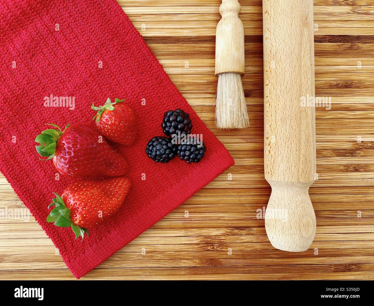 Strawberries and blackberries on a wooden kitchen counter. Ingredients for baking a summer berry, strawberry and blackberry pie. - Smartphone Captured Stock Image