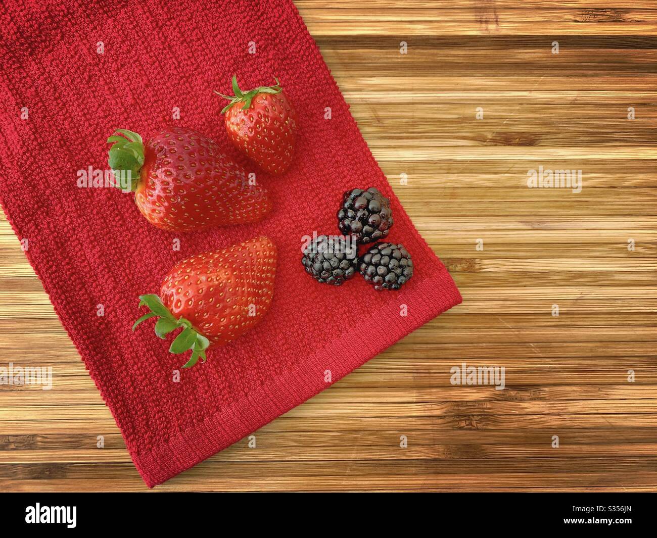 Strawberries and blackberries on a wooden kitchen counter. Ingredients for baking a summer berry, strawberry and blackberry pie. - Smartphone Captured Stock Image