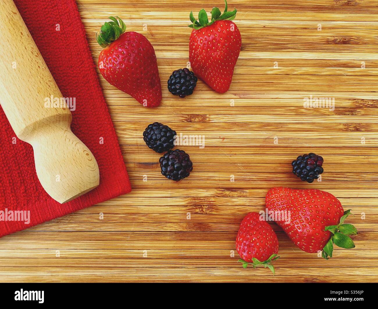 Strawberries and blackberries on a wooden kitchen counter. Ingredients for baking a summer berry, strawberry and blackberry pie. - Smartphone Captured Stock Image