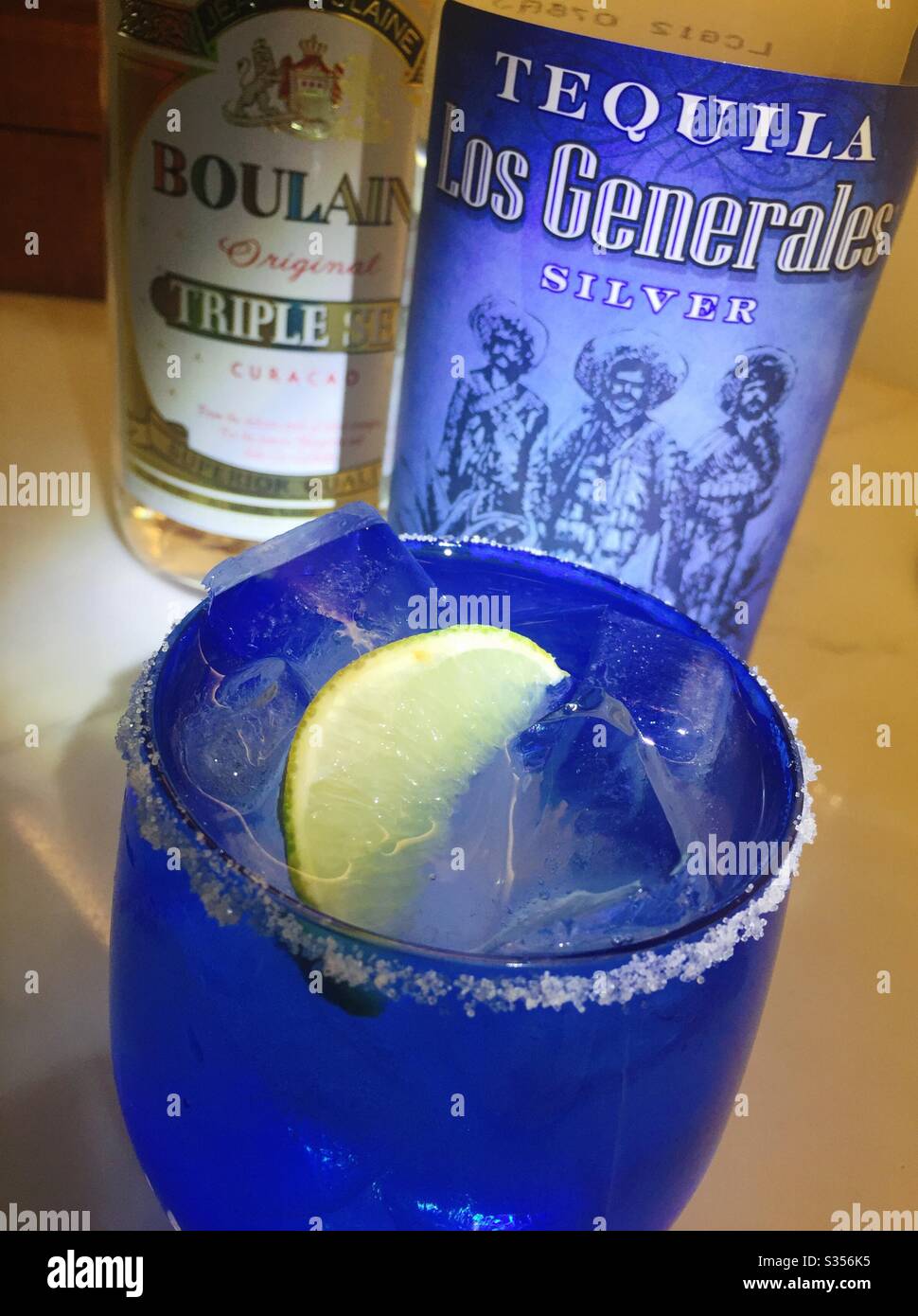 A margarita cocktail with a salted rim on the rocks in front of a bottle of tequila and a bottle