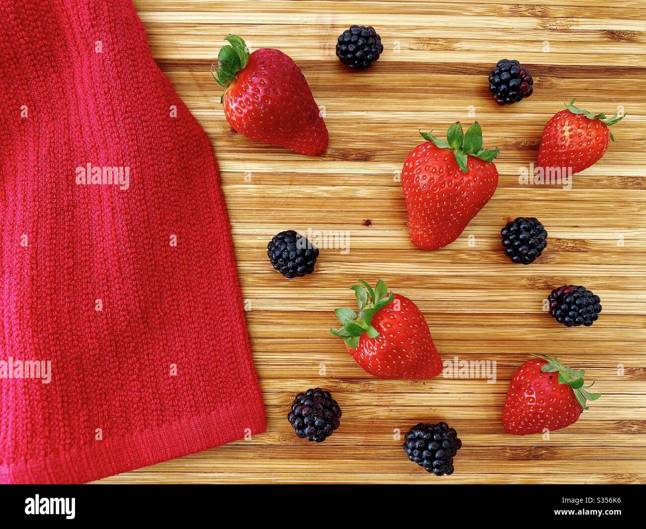 Strawberries and blackberries on a wooden kitchen counter. Ingredients for baking a summer berry, strawberry and blackberry pie. - Smartphone Captured Stock Image